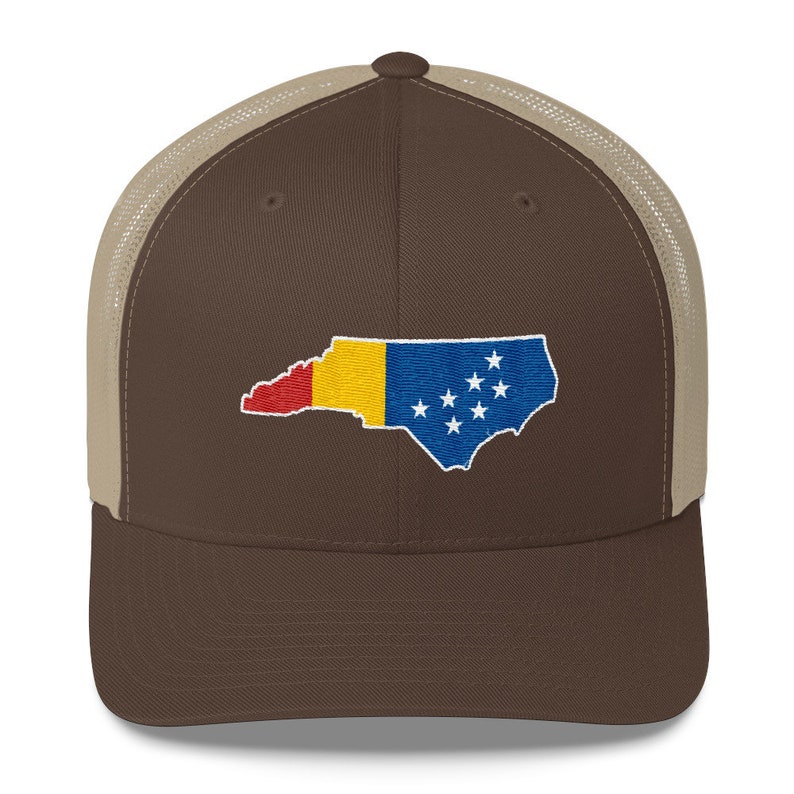 May include: A brown and tan trucker hat with an embroidered outline of the state of North Carolina, filled with the colours of the North Carolina flag.