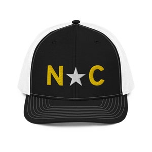 May include: Black and white trucker hat with a gold embroidered "N*C" logo.
