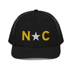 May include: Black mesh trucker hat with a white star and the letters "N*C" in yellow embroidery.