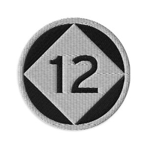 Op de afbeelding: Een witte en zwarte ronde patch met een ruitvorm in het midden. De ruit heeft een zwarte omtrek en het getal "12" in zwarte tekst.