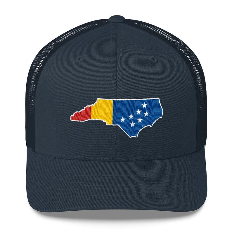 May include: A navy blue trucker hat with a mesh back. The front of the hat features an embroidered outline of the state of North Carolina with the state flag colours.