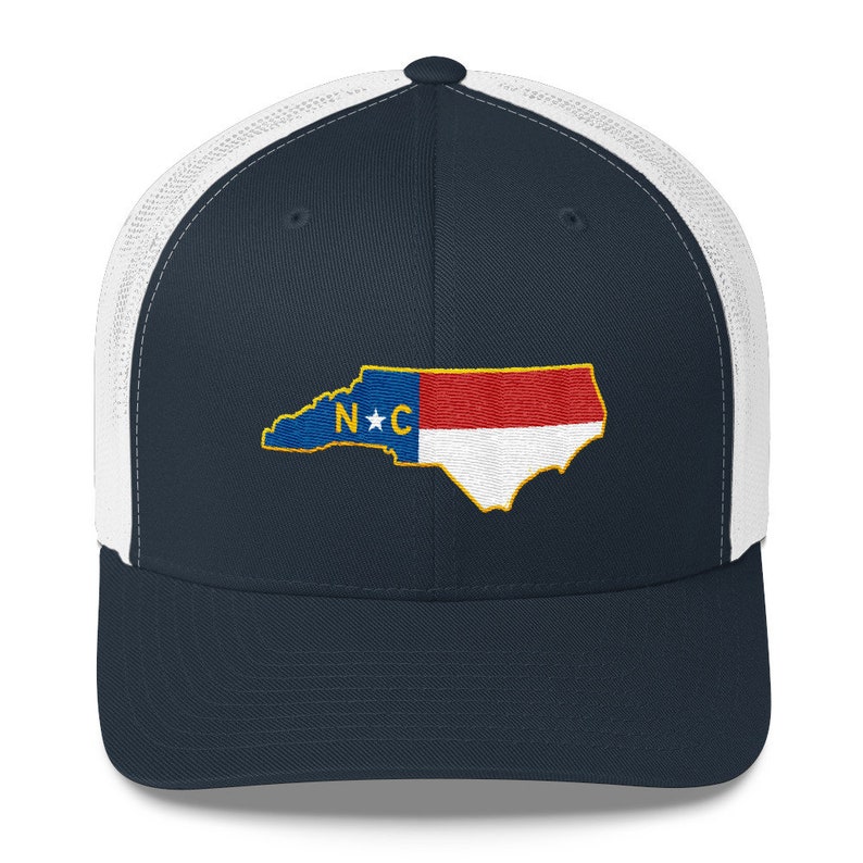 May include: A navy blue and white trucker hat with an embroidered North Carolina state outline and flag. The flag features a red and white stripe with a blue star and the letters "N*C" in the center.