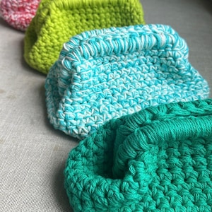 Può includere: Quattro pochette all'uncinetto in diversi colori: rosa, verde, blu e turchese. Le pochette sono allineate in una fila, con la pochette rosa in alto e la pochette turchese in basso.