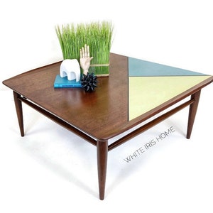 May include: Mid-century modern coffee table with a wood top and a geometric design in blue, green, and yellow. The table has four tapered legs.
