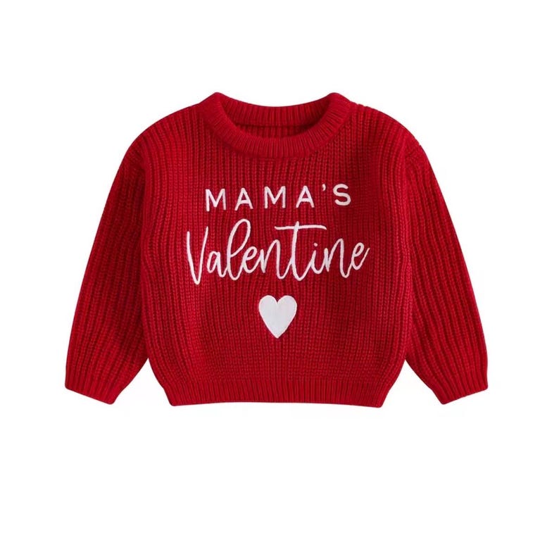 May include: A red knit sweater with long sleeves. The sweater features the text "MAMA'S Valentine" in white script, with a white heart below the text. The sweater is designed for children.