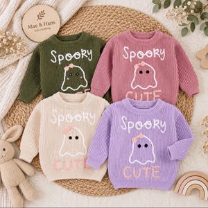 Puede incluir: Cuatro jerséis de punto de manga larga en verde oliva, rosa empolvado, crema y lavanda. Cada jersey presenta un gráfico de fantasma bordado en blanco con un pequeño lazo rosa y el texto "Spooky" arriba y "CUTE" debajo del diseño.