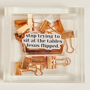 May include: A clear acrylic box filled with rose gold binder clips. A white sticker with black text reads "stop trying to sit at the tables Jesus flipped."