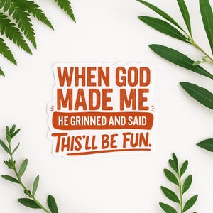 May include: A white sticker with the text "WHEN GOD MADE ME HE GRINNED AND SAID THIS'LL BE FUN" in orange lettering. Green leaves are in the background.
