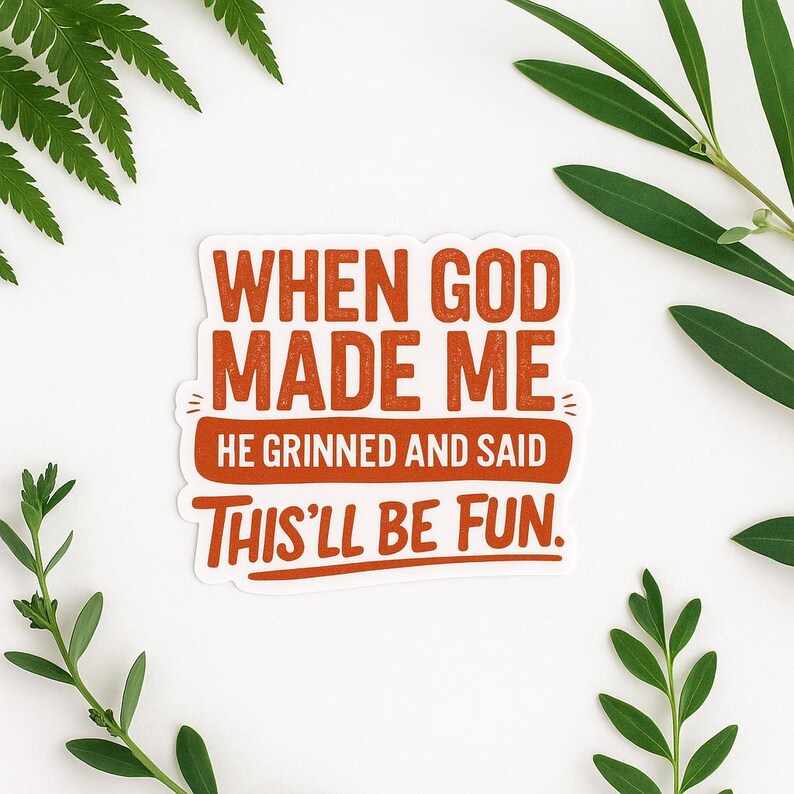 May include: A white sticker with the text "WHEN GOD MADE ME HE GRINNED AND SAID THIS'LL BE FUN" in orange lettering. Green leaves are in the background.