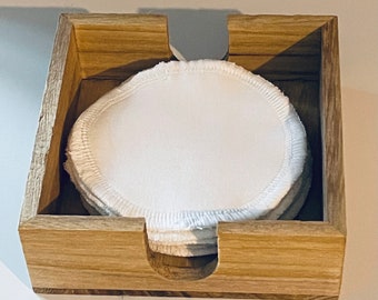 Puede incluir: Una caja de madera con una pila de discos de algodón blancos en su interior. La caja tiene un recorte en la parte delantera para permitir que los discos se retiren fácilmente.