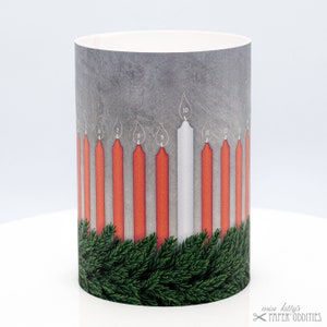 Könnte beinhalten: Zylindrischer Papier-Adventskalender mit grauem Hintergrund und roten Kerzen, bis auf eine weiße Kerze. Die Kerzen sind nummeriert. Grüne Tannenzweige befinden sich am unteren Rand. Der Text "miss kitty's PAPER ODDITIES" befindet sich unten rechts.