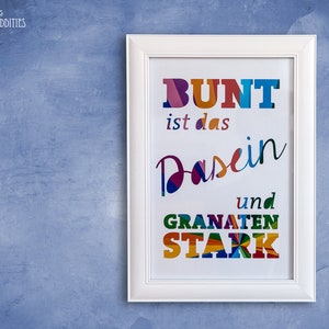 Könnte beinhalten: Ein weißer gerahmter Druck mit dem Text "BUNT ist das Dasein und GRANATEN STARK" in bunten, übereinanderliegenden Papierbuchstaben.