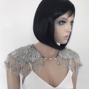 May include: A silver beaded bridal shawl with a floral design and fringe. The shawl is made of delicate beads and sequins and is perfect for adding a touch of sparkle to any wedding dress.