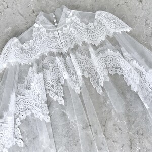 May include: A white lace bridal veil with a scalloped edge and delicate floral patterns. The veil is made of soft tulle and has a delicate, romantic feel.