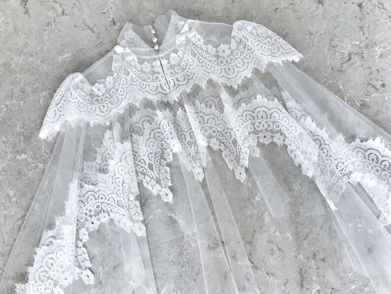 May include: A white lace bridal veil with a scalloped edge and delicate floral patterns. The veil is made of soft tulle and has a delicate, romantic feel.