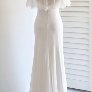 May include: A white wedding dress with a long, flowing skirt and a lace bodice. The dress has a sheer, layered cape with pearl embellishments.