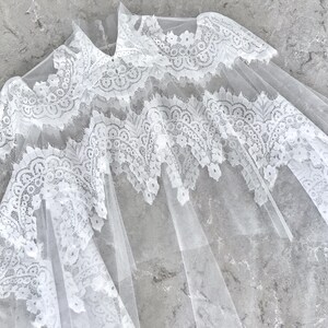 May include: White lace overlay with a delicate floral pattern. The lace is sheer and has a soft, flowing texture.