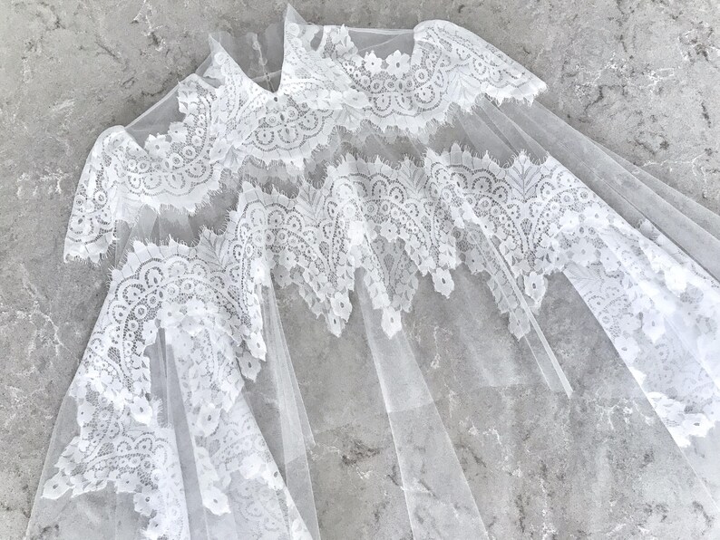 May include: White lace overlay with a delicate floral pattern. The lace is sheer and has a soft, flowing texture.