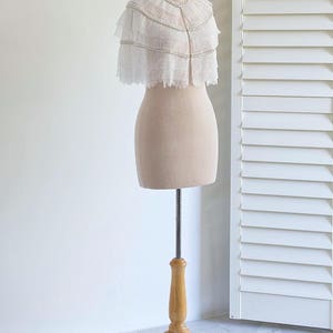 May include: A white lace bridal cape with pearl embellishments, displayed on a wooden mannequin stand.