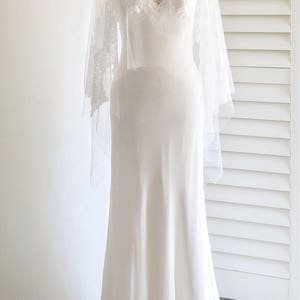 May include: A white wedding dress with a lace overlay and a high neckline. The dress has a fitted bodice and a flowing skirt.