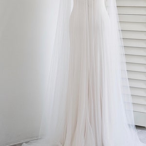 May include: A white tulle wedding cape with a beaded embellishment around the neckline.