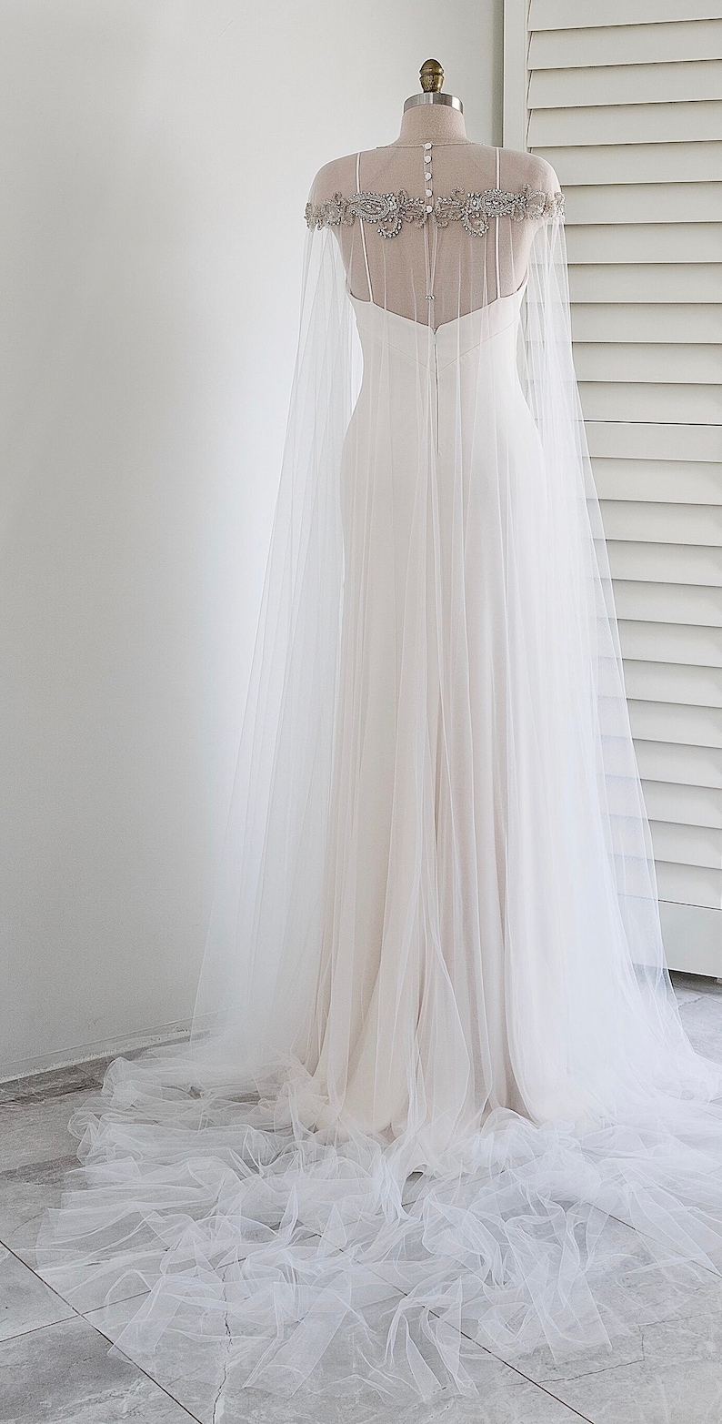May include: A white tulle wedding cape with a beaded embellishment around the neckline.