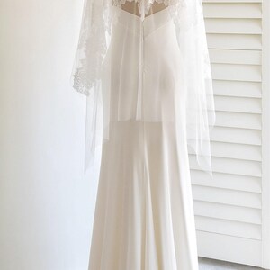 May include: A white wedding dress with a lace overlay and long sleeves. The dress has a fitted bodice and a flowing skirt.