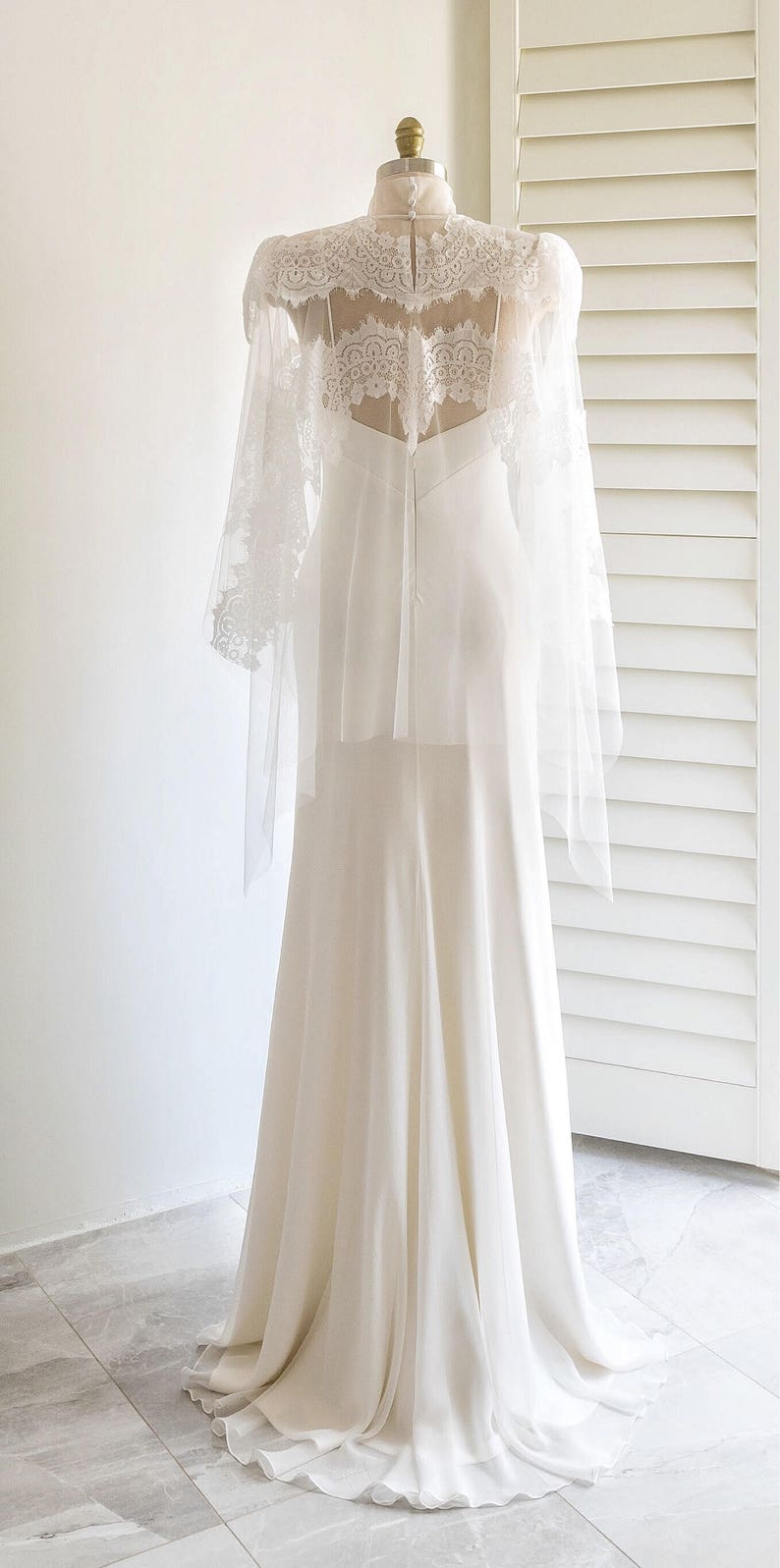 May include: A white wedding dress with a lace overlay and long sleeves. The dress has a fitted bodice and a flowing skirt.
