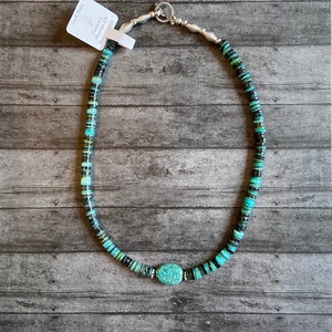 May include: A turquoise and black beaded necklace with a silver clasp and a large turquoise pendant. The necklace is handmade in Santa Fe, New Mexico.