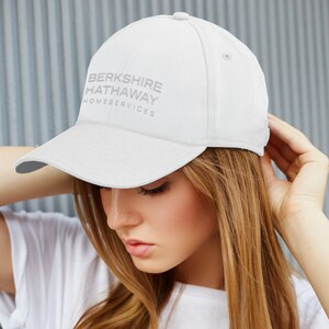 May include: White baseball cap with the text "BERKSHIRE HATHAWAY HOMESERVICES" embroidered in gray on the front.