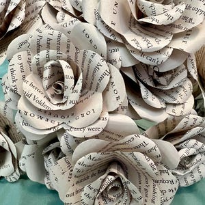 May include: A bouquet of paper roses crafted from book pages. The roses are white with visible text, creating a unique and literary aesthetic. The petals are carefully shaped to resemble real roses.