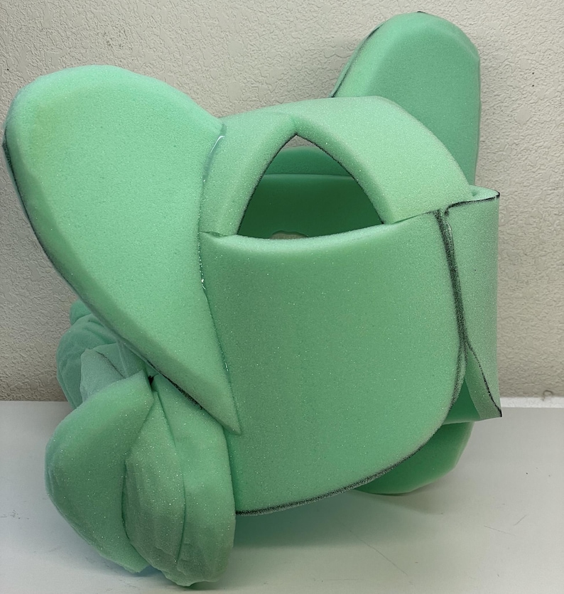 May include: A green foam head form with two large ears, a cut-out for the face, and markings for sewing.