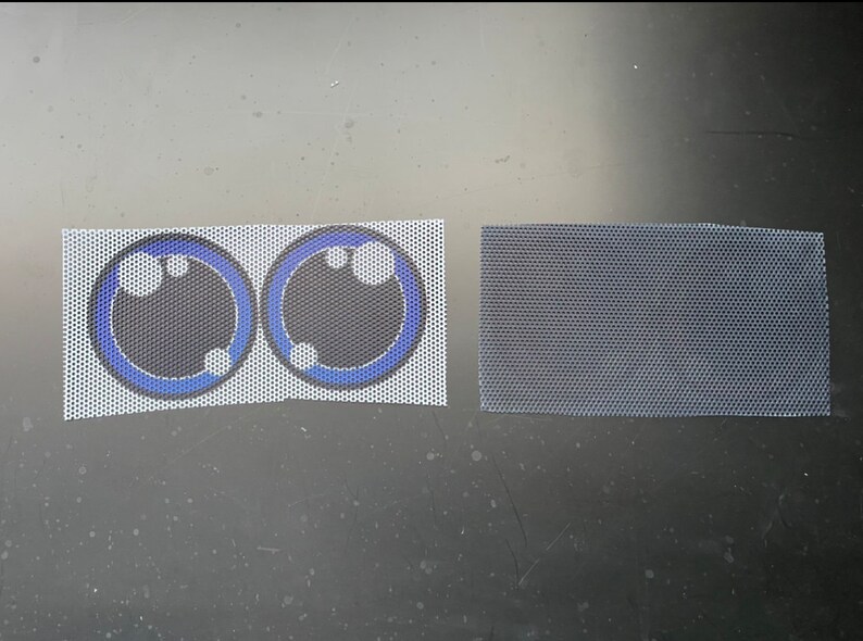 May include: Two white mesh fabric patches with blue and black printed eyes. The eyes have a black center, a blue ring, and three white dots.