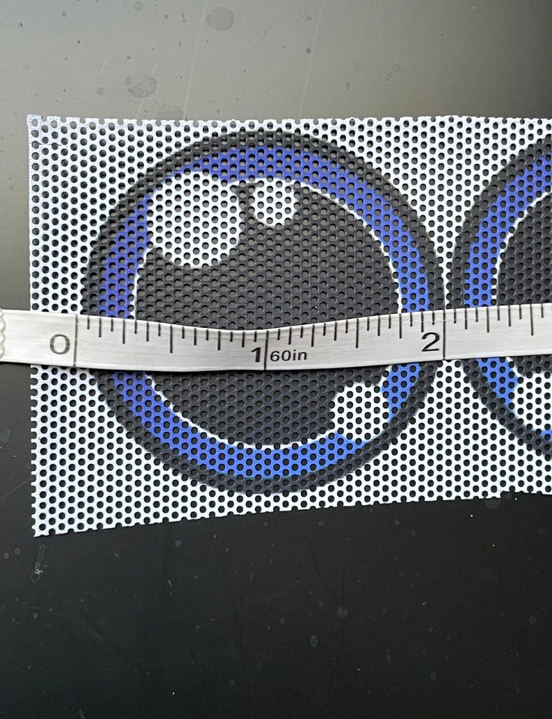May include: A close-up of a white mesh fabric with two blue and black circles printed on it. The fabric is measured with a ruler, showing 1 1/2 inches.