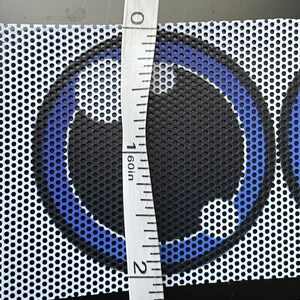 May include: A close-up of a white mesh fabric with a blue and black circular design. A ruler is placed next to the fabric, measuring 1 inch.