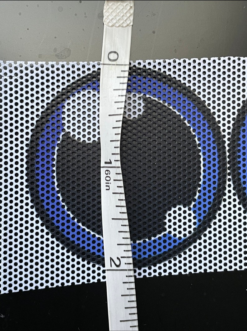 May include: A close-up of a white mesh fabric with a blue and black circular design. A ruler is placed next to the fabric, measuring 1 inch.