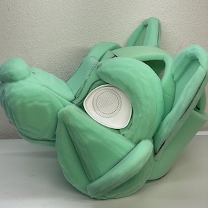 May include: A green foam head for a furry costume with a white mesh eye piece.