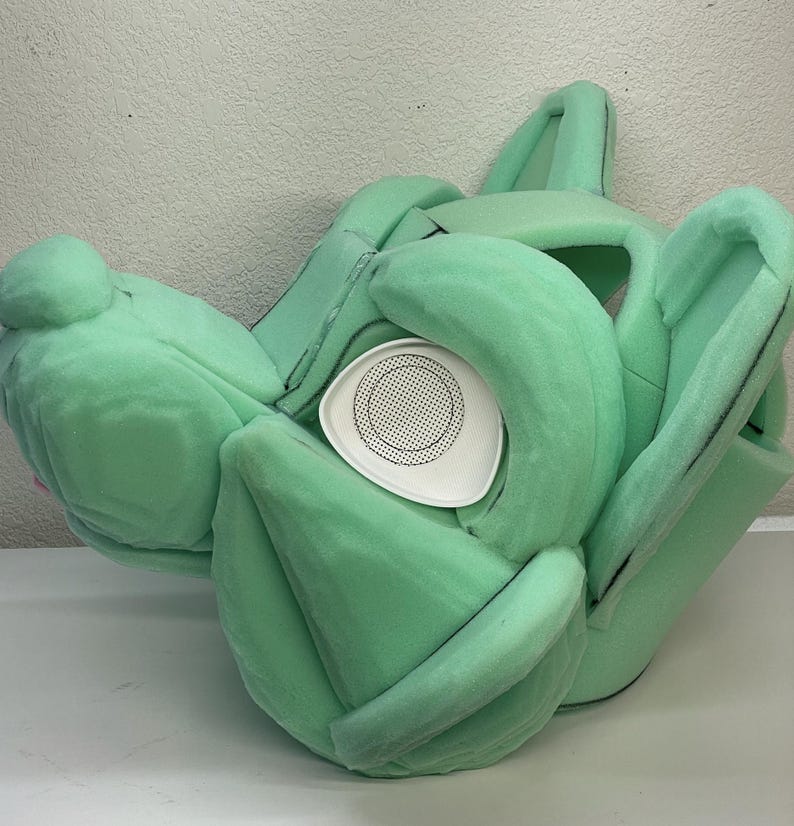 May include: A green foam head for a furry costume with a white mesh eye piece.