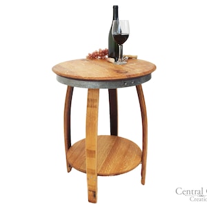 May include: A round wooden end table made from a reclaimed wine barrel with a metal band around the top. The table has a lower shelf and is shown with a bottle of wine and a glass of wine on the top.