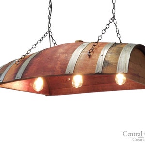 May include: A rustic wooden wine barrel chandelier with a curved design and three light bulbs. The barrel is made of reclaimed wood and has metal bands around it.