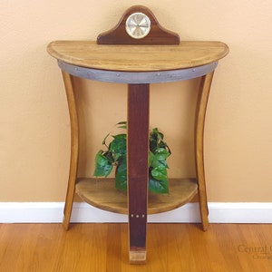 May include: A half-barrel table with a clock on top and a shelf underneath. The table is made of wood and has a natural finish. The clock is round and has a silver face. The shelf is made of wood and has a natural finish.