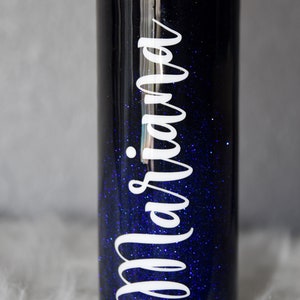 May include: A black and blue glitter tumbler with the name "Mariana" written in white on the side.