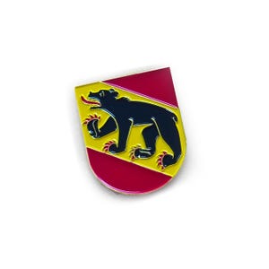 May include: A shield-shaped enamel pin featuring a black bear on a yellow background, with red borders and accents. The bear has red claws and tongue. The pin is a collectible item.