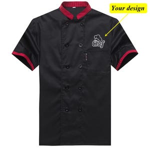 May include: Black chef's coat with short sleeves and a double-breasted front. The collar and sleeve cuffs have a red striped trim. A white embroidered chef's hat and the word "Chef" are on the chest. The text "Your design" is in the upper right corner.