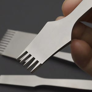 Pode incluir: Close-up de várias ferramentas de costura em couro de aço inoxidável. As ferramentas têm uma alça plana e larga e uma borda dentada para criar furos espaçados uniformemente. Ferramentas para artesanato em couro e projetos semelhantes.