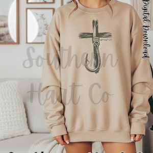 K&ouml;nnte beinhalten: Ein beigefarbenes Sweatshirt mit Rundhalsausschnitt und einem dunkelgr&uuml;nen Grafikdruck, der ein Kreuz mit einem Angelhaken kombiniert. Das Design enth&auml;lt den Text Matthew 4:19 in der N&auml;he des Hakens. Das Sweatshirt hat lange &Auml;rmel sowie gerippte B&uuml;ndchen.