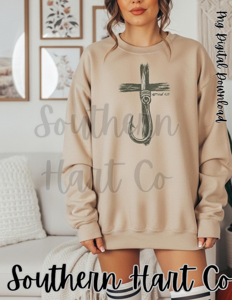 K&ouml;nnte beinhalten: Ein beigefarbenes Sweatshirt mit Rundhalsausschnitt und einem dunkelgr&uuml;nen Grafikdruck, der ein Kreuz mit einem Angelhaken kombiniert. Das Design enth&auml;lt den Text Matthew 4:19 in der N&auml;he des Hakens. Das Sweatshirt hat lange &Auml;rmel sowie gerippte B&uuml;ndchen.