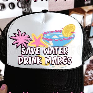 May include: Black and white trucker hat with a white front panel featuring a margarita graphic, palm tree, and the text "SAVE WATER DRINK MARGS". The hat also has the text "Southern Hart Co".