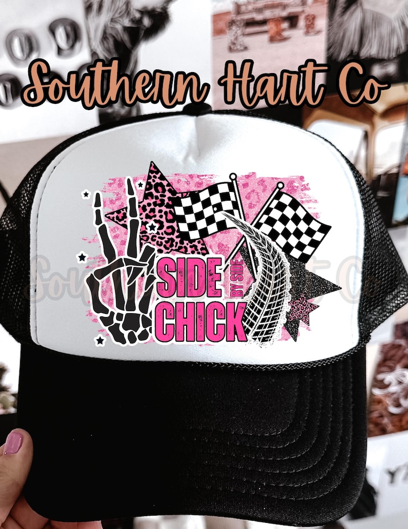 May include: Black and white trucker hat with a white front panel featuring a pink and black graphic. The graphic includes a skeleton hand, checkered flags, and the words "SIDE CHICK". The hat has a black brim and mesh back.