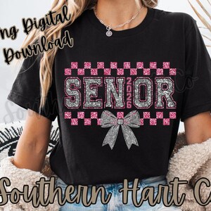 Puede incluir: Camiseta negra con un diseño brillante "SENIOR 2026" en plata y rosa. El diseño incluye un lazo y un patrón de cuadros. La camiseta es una descarga digital.